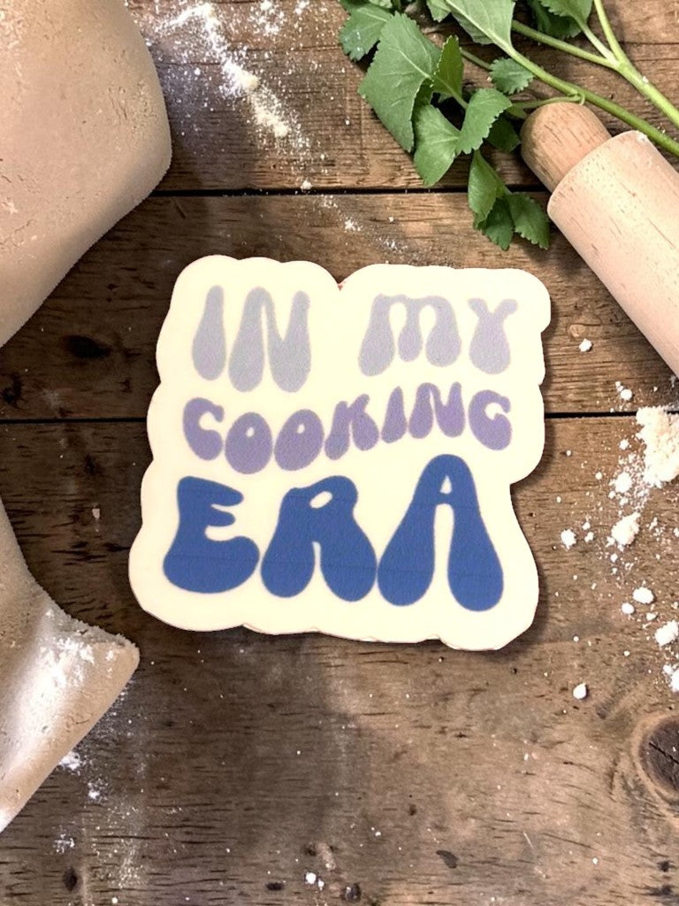 Permanent Sticker with 'In my cooking era' text on a wooden surface with flour and herbs.