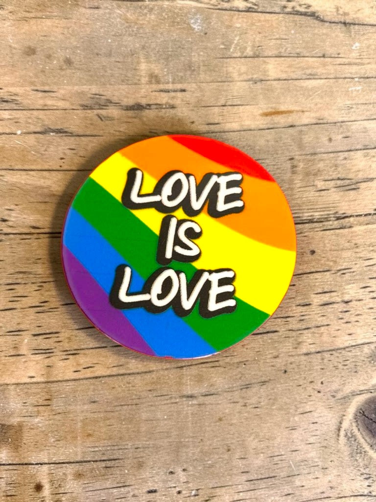 Round rainbow permanent sticker with 'LOVE IS LOVE' text on a wooden surface