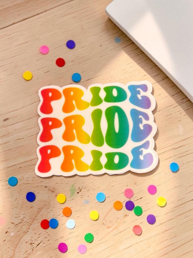 Rainbow 'PRIDE' permanent sticker on a wooden surface with confetti