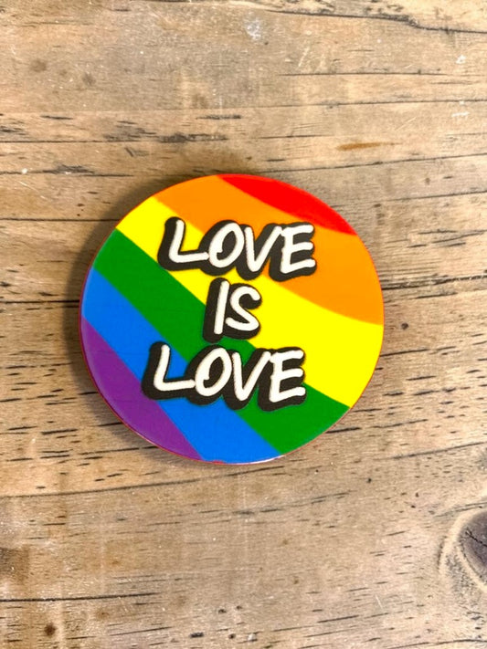 Round rainbow permanent sticker with 'LOVE IS LOVE' text on a wooden surface