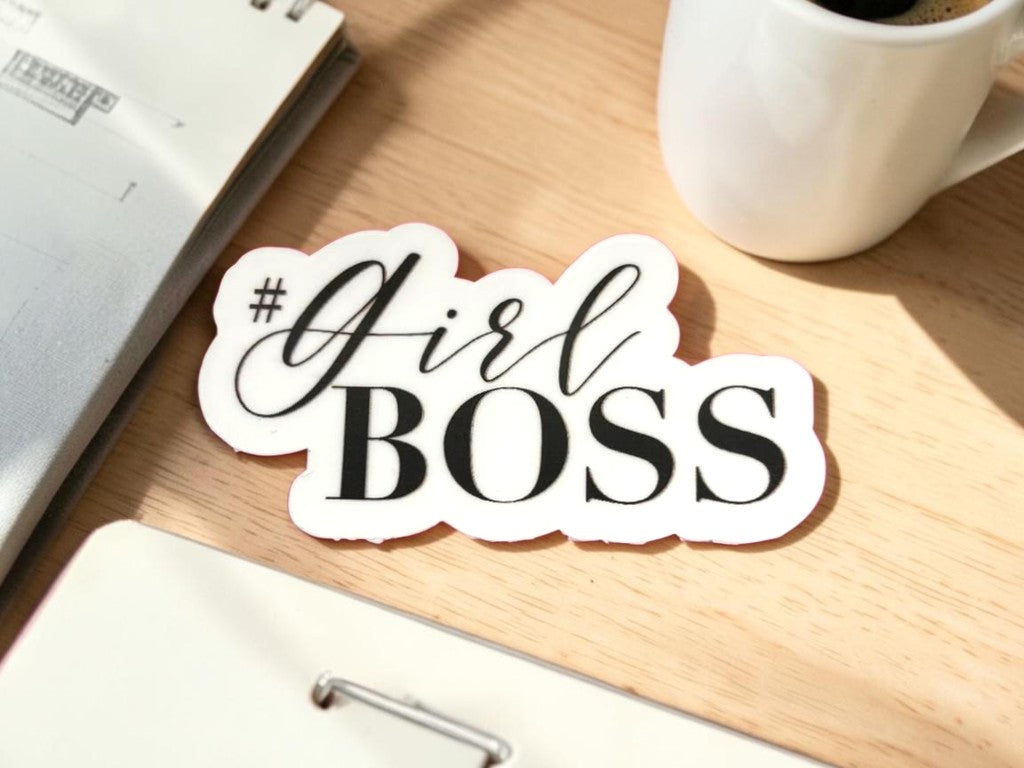 permanent sticker with 'Girl Boss' text on a desk with a coffee cup and notebook.