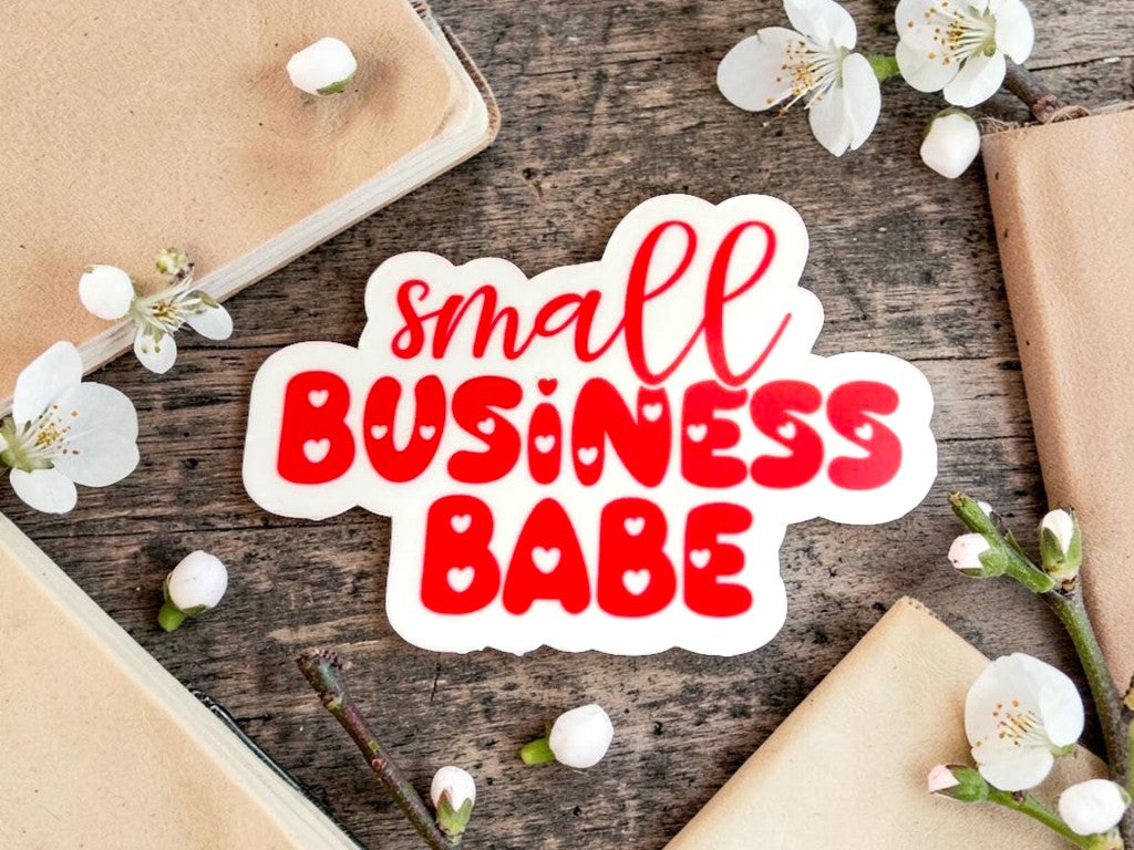 Permanent sticker with 'small BUSINESS BABE' text on a wooden surface with flowers